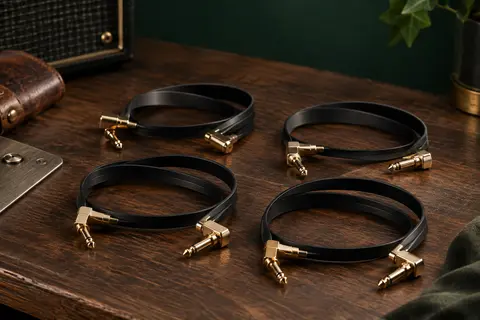 Quatre câbles patch plats noirs à fiches plaquées or posés sur un établi de musicien