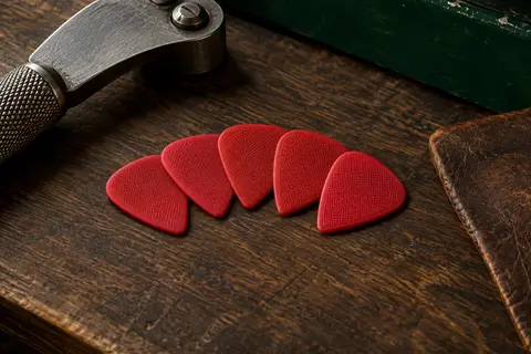 Six médiators rouges en nylon au profil Jazz III et à la surface Max-Grip texturée, posés sur un établi.