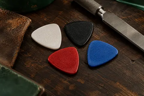 Médiators de guitare en nylon à surface texturée, présentés en blanc, noir, rouge et bleu sur un établi.