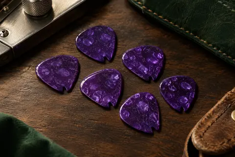 Médiators Dunlop Jazz III en celluloïd violet brillant, avec une encoche en V, posés sur un établi en bois sombre.