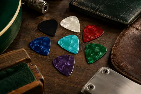 Médiators 351 en celluloïd de couleurs variées disposés sur un établi de musicien sombre.