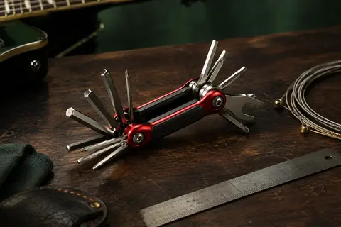 Multi-outil Fender rouge et métal avec clés hexagonales, tournevis et douille posé sur un établi sombre.