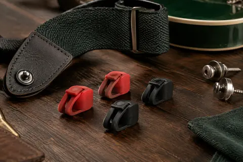 Quatre bloqueurs de sangle Fender, deux rouges et deux noirs, posés sur un établi de musicien