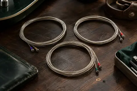 Trois jeux de cordes électriques en acier nickelé, avec extrémités à boule, posés sur un établi sombre.