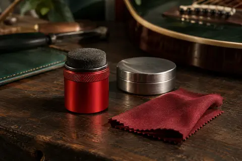Applicateur rouge de lubrifiant pour cordes avec son chiffon, posé sur un établi de musicien en bois sombre.