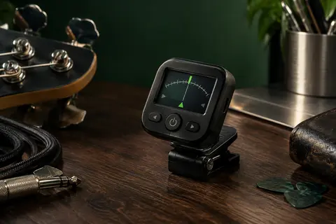 Accordeur électronique noir pour guitare et basse posé sur un établi de musicien en bois sombre