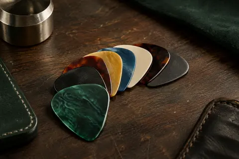 Assortiment de médiators colorés aux bords arrondis disposés sur un établi en bois sombre.