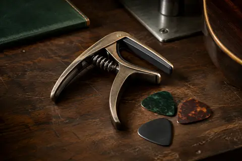 Capodastre Takit en zinc bronze avec pad en silicone et trois médiators sur un établi sombre.