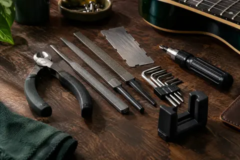 Kit d’outils de réglage pour guitare en métal argenté et plastique noir posé sur un établi en bois sombre.