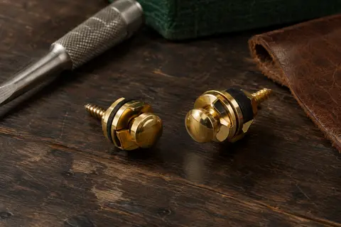 Deux verrous de sangle métalliques dorés pour guitare posés sur un établi en bois sombre